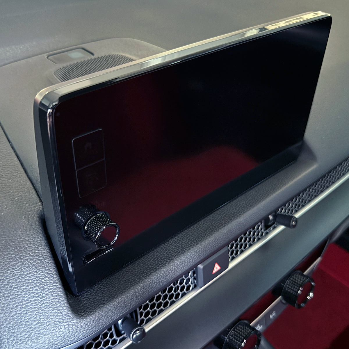 A close-up of a gloss black radio knob for a Honda 9" infotainment screen with a chrome bezel, mounted on a textured gray dashboard with a rotary controller below it.