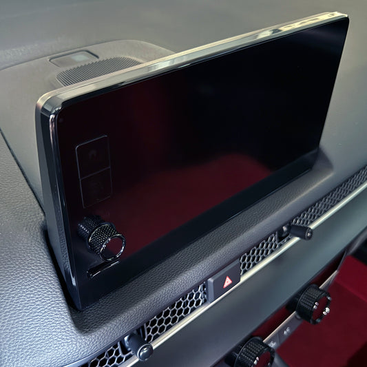 A close-up of a gloss black radio knob for a Honda 9" infotainment screen with a chrome bezel, mounted on a textured gray dashboard with a rotary controller below it.