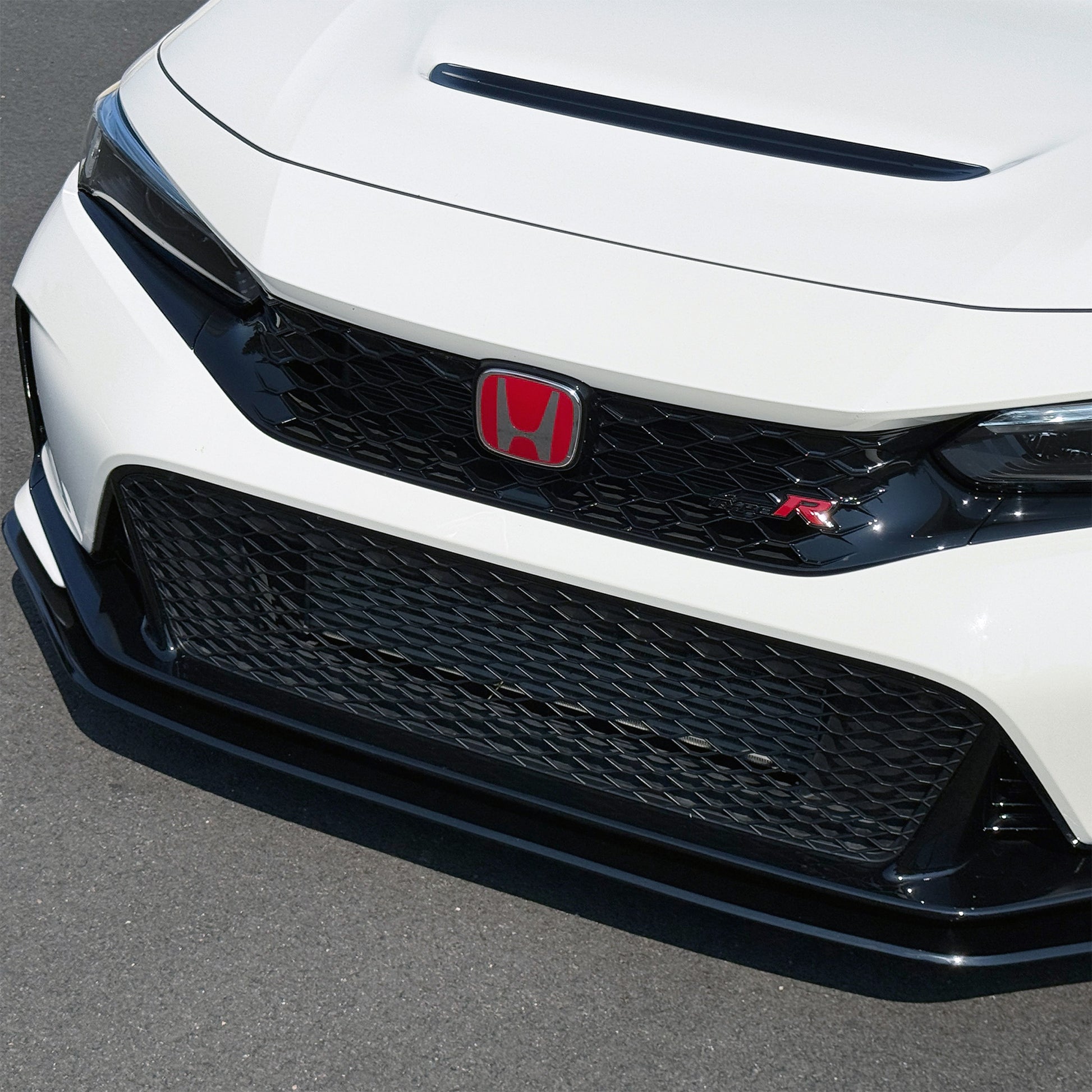 Close-up of the front grille and lower bumper of a Championship White Honda Civic Type R FL5 showing the black honeycomb grille, red Honda logo, and Project Aero black lip spoiler on an asphalt surface.
