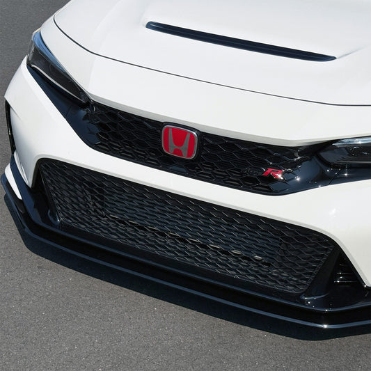 Close-up of the front grille and lower bumper of a Championship White Honda Civic Type R FL5 showing the black honeycomb grille, red Honda logo, and Project Aero black lip spoiler on an asphalt surface.
